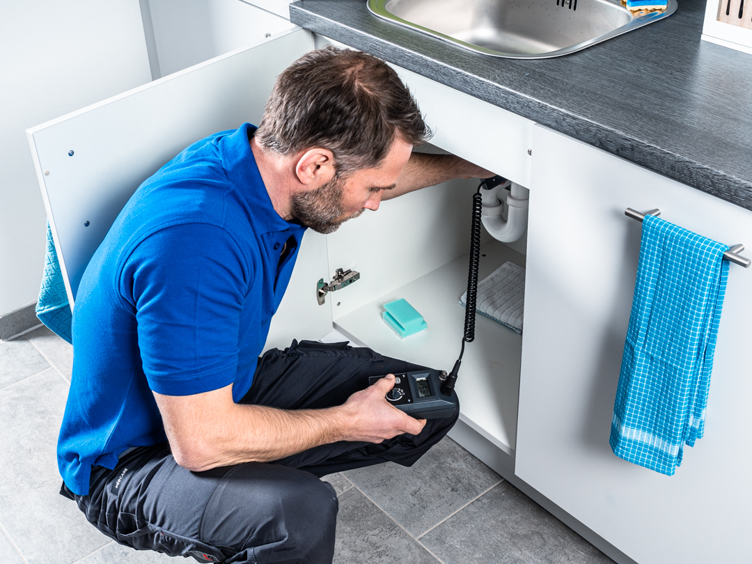 LOCATEC Messtechniker untersucht eine Leitung unter der Spüle zur Leckortung in einem Gebäude.